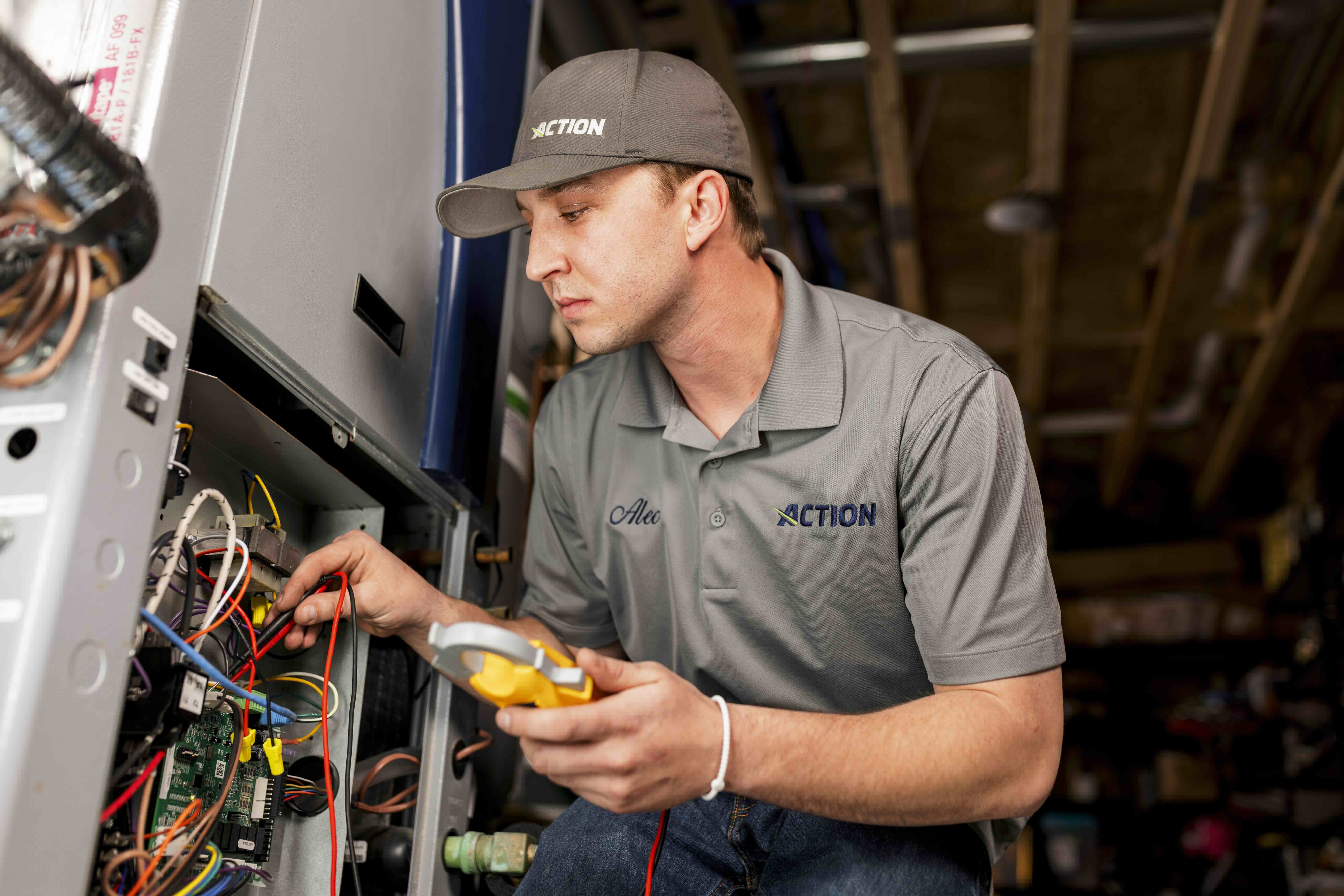 Action technician in a gray uniform and cap removing an air filter from an HVAC furnace unit during a service visit.